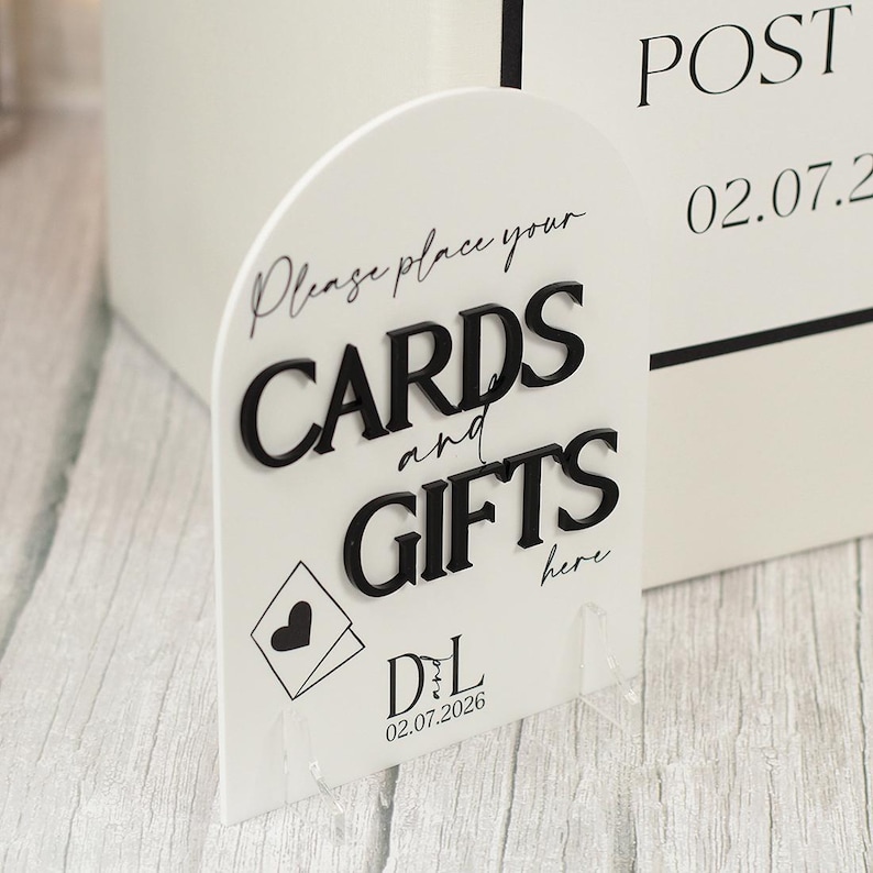 May include: An arched white acrylic sign featuring raised black lettering that reads "Please place your CARDS and GIFTS here". The sign includes a black envelope icon with a heart, the initials "DL", and the date "02.07.2026" printed in black.