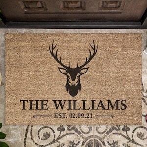 May include: A brown coir doormat with a black silhouette of a deer head and antlers. The text "THE WILLIAMS EST. 02.09.21" is printed below the deer.