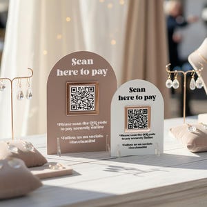 May include: Two arched payment signs with QR codes. The larger sign is dusty rose with white text, and the smaller is white with black text. Both read: Scan here to pay, Please scan the QR code to pay securely online, Follow us on socials: @lovelumiltd.