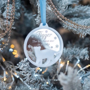 May include: White round Christmas bauble with a blue ribbon. The bauble has a cat silhouette and the text "Tigger The brightest star in the sky".