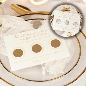 May include: A wedding scratch card with gold text saying "Thank you for sharing our special day." The card features three scratch-off areas and a message to claim a free drink. It rests on a white plate with gold edging.