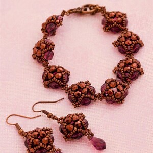 Könnte beinhalten: Ein Schmuckset aus lila und kupferfarbenen Perlen mit einem Armband und Ohrringen. Das Armband besteht aus kleinen, facettierten Perlen in einem geometrischen Muster. Die Ohrringe sind Ohrhänger mit einem ähnlichen Perlenmuster.