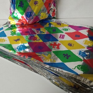Puede incluir: Una pila de bolsas de regalo de papel de aluminio plateado y coloridas con un patr&oacute;n repetitivo de varias formas y s&iacute;mbolos. Las bolsas est&aacute;n dobladas y apiladas unas sobre otras.