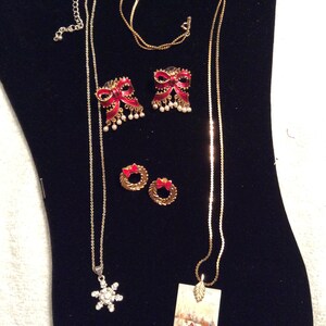 Peut inclure: Un ensemble de bijoux sur le thème de Noël comprenant un collier en chaîne dorée avec un pendentif flocon de neige, un collier en chaîne dorée avec un petit pendentif maison, une paire de boucles d'oreilles en forme de nœud rouge et une paire de boucles d'oreilles en forme de couronne dorée.