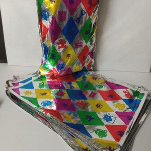 Puede incluir: Una pila de hojas de papel de regalo de aluminio plateado y colorido con un patr&oacute;n de diamantes y varias im&aacute;genes de dibujos animados. El papel de regalo presenta una variedad de colores, incluyendo rojo, amarillo, azul, verde y morado.