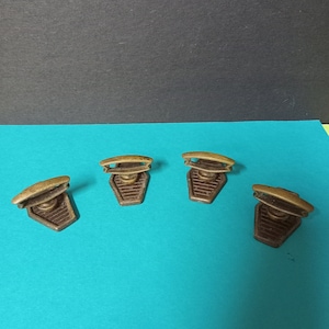 May include: Four antique brass cabinet door pulls with a brown wooden base. The pulls are in the shape of a half-circle with a raised centre.