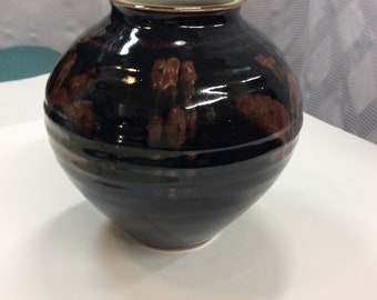 Könnte beinhalten: Eine dunkelbraune Keramikvase mit glänzender Oberfläche und einem dezenten roten Muster. Die Vase hat eine abgerundete Form und eine breite Öffnung.