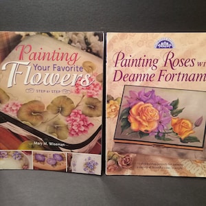 May include: Two books on painting flowers. The book on the left is titled "Painting Your Favorite Flowers Step by Step" by Mary M. Wiseman. The book on the right is titled "Painting Roses with Deanne Fortnam MDA".