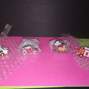 Può includere: Quattro veicoli giocattolo in miniatura: un'auto della polizia, un'auto rossa, un treno e un camion dei pompieri. L'auto della polizia è bianca e blu, l'auto rossa ha ruote blu, il treno è rosso e giallo, e il camion dei pompieri è rosso con le lettere "FD".