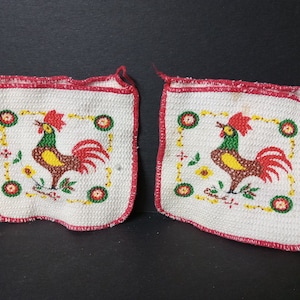 May include: Two white cotton pot holders with red trim and a rooster design. The roosters are green, yellow, and brown with red combs and wattles.