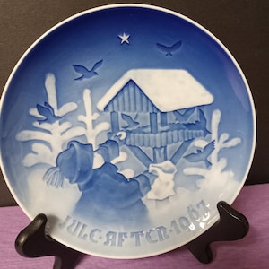 Könnte beinhalten: Ein blauer und weißer Keramikteller mit einem Reliefdesign einer Vogeltränke und einer Person, die sie mit Vogelfutter füllt. Der Teller trägt den Text "JULGAFTER 1961" auf der Unterseite.