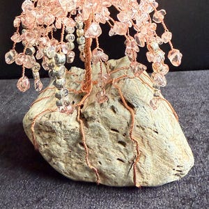 May include: A pink crystal wire wrapped tree sculpture with copper wire branches and a natural wood base.