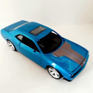 May include: A blue toy car with a brown stripe down the hood. The car has a sunroof and white wheels. The car is a model of a sports car.