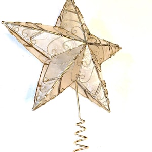 May include: A five-pointed star tree topper featuring a gold wire frame with intricate swirling patterns and translucent off-white panels. The star is attached to a gold-colored metal coil base designed for securing the ornament to a tree top.