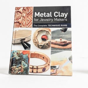 May include: A softcover book titled Metal Clay for Jewelry Makers: The Complete TECHNIQUE GUIDE. The cover features a collage of six images showing various metal clay jewelry projects, including a ring, a pendant, and textured metal pieces.