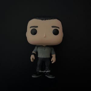 以下が含まれることがあります： ニュートラルな表情の人物のFunko Popビニールフィギュア。グレーのシャツと黒いパンツを着用しています。フィギュアは黒い髪と大きな黒い目を持っています。フィギュアは黒い表面に立っています。フィギュアの名前は「Havenbornfall's」です。