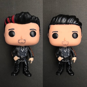 May include: Two black and white pop vinyl figures with black hair and facial hair. One figure has a red and black stripe on the side of their head. Both figures are wearing black jackets with silver accents and black pants.