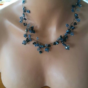 Könnte beinhalten: Eine zarte Halskette aus schwarzem Draht mit blauen und klaren Kristallperlen. Die Halskette ist in einem kaskadierenden Muster angeordnet, das einen verspielten und eleganten Look erzeugt.