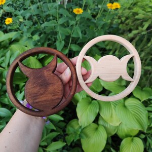 May include: Two circular wooden wall hangings, one in a dark brown finish and one in a light natural wood finish. The dark piece features a cutout of a bull symbol, while the light piece features a cutout of a triple moon symbol.