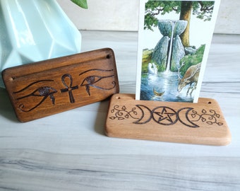 Puede incluir: Dos soportes de tarjetas de madera con tallas intrincadas. El primer soporte presenta un ojo de Horus y un símbolo Ankh. El segundo soporte tiene un símbolo de triple luna y un pentagrama.