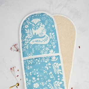 May include: A blue oven mitt with a white fox and floral pattern on one side and a white terry cloth on the other side.