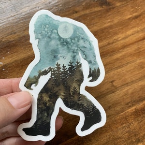 Op de afbeelding: Een aquarel sticker van Bigfoot die door een bos loopt met een volle maan op de achtergrond.