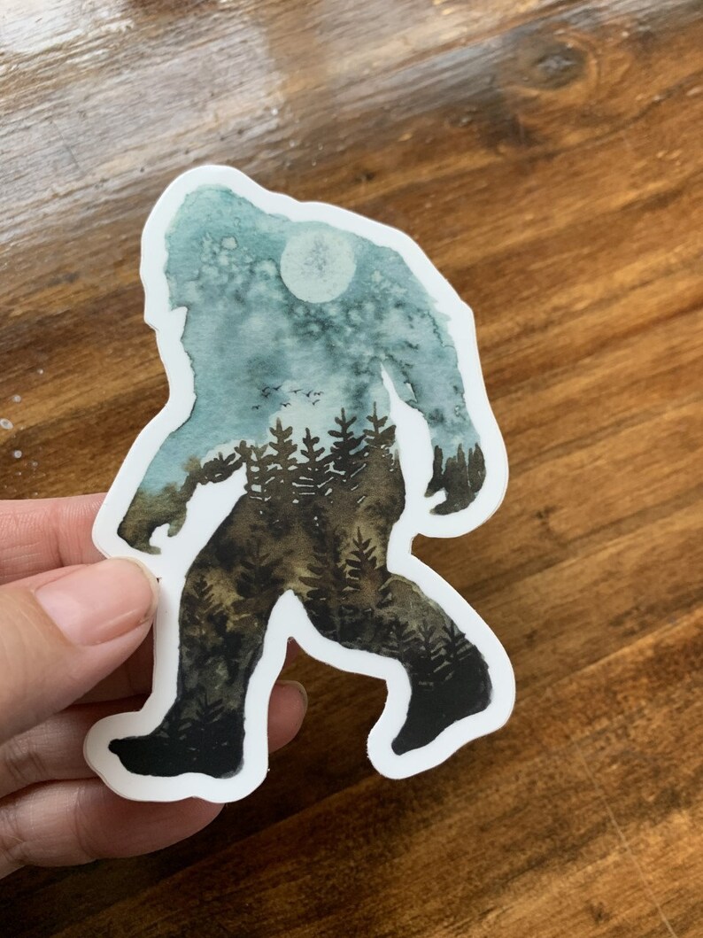 Op de afbeelding: Een aquarel sticker van Bigfoot die door een bos loopt met een volle maan op de achtergrond.