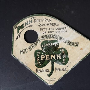 May include: A white metal pot and pan scraper with a hole in the center. The scraper is shaped like a shamrock and has the text "Penn Pot and Pan Scraper" and "Mt Penn Stove Works" printed on it.