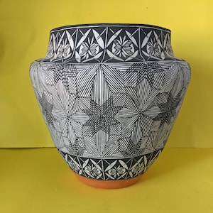 May include: A black and white ceramic vase with a geometric pattern. The vase has a wide base and a narrow neck.