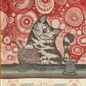 May include: A red and white kitchen towel with a gray cat holding a ball of yarn. The cat is sitting on a table with a spool of thread. The towel has a border with the words "MIAO &hearts; MIAO" and two small cats.