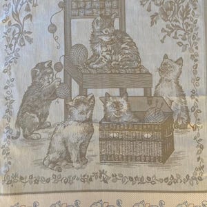 Peut inclure: Une tapisserie beige repr&eacute;sentant une sc&egrave;ne de quatre chatons jouant avec des pelotes de laine. Les chatons sont dans diff&eacute;rentes positions, l'un assis sur une chaise, l'autre dans un panier et les deux autres sur le sol. La tapisserie a une bordure florale et une bordure inf&eacute;rieure de paniers tiss&eacute;s.