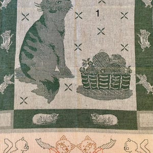 Peut inclure: Une serviette de cuisine verte et blanche avec un chat, un panier de laine et le chiffre "1" brod&eacute; dessus. La serviette a une bordure de carr&eacute;s verts et blancs.