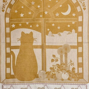 May include: A beige kitchen towel with a brown cat looking out a window with stars and a crescent moon. The window is framed in brown and has a white background. The towel has a border of brown and white squares. The bottom of the towel has a row of five brown cats with hearts.
