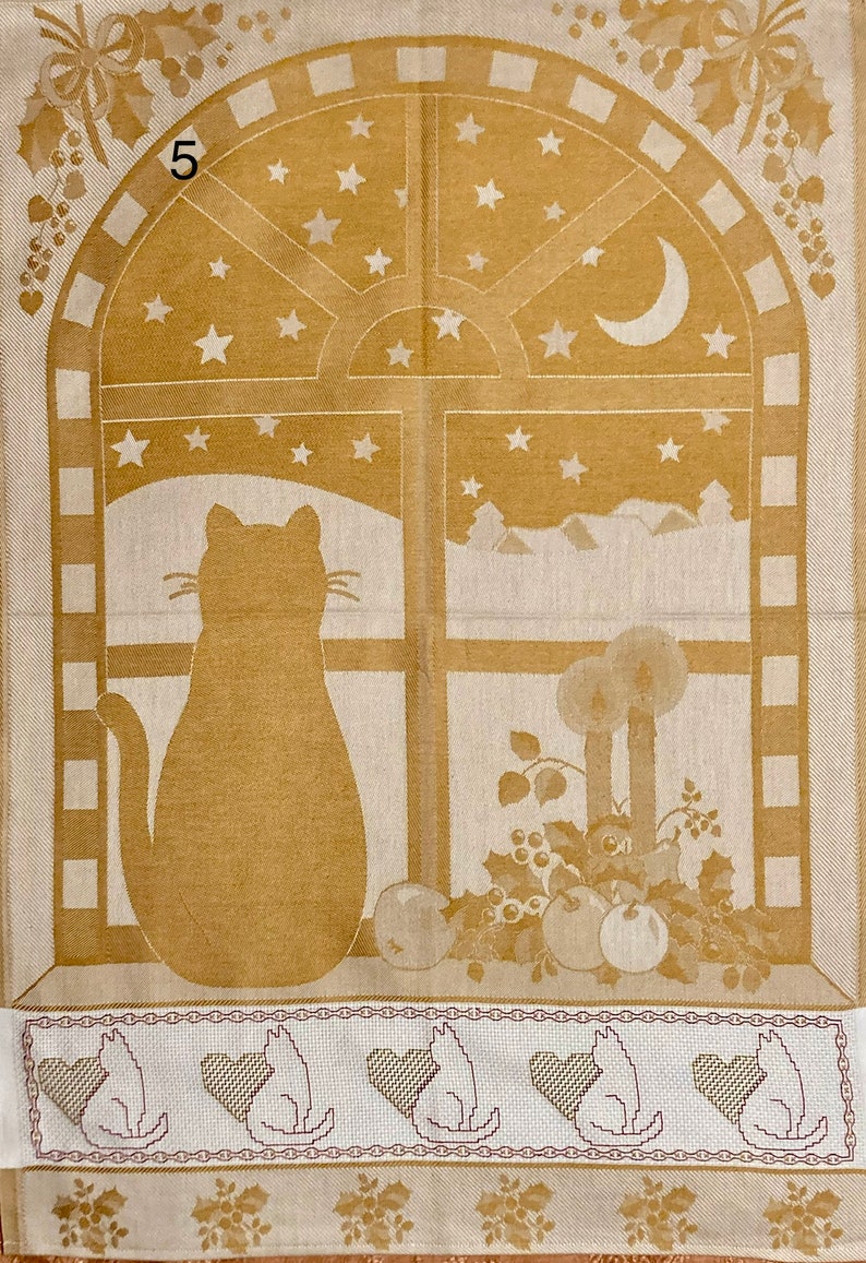 May include: A beige kitchen towel with a brown cat looking out a window with stars and a crescent moon. The window is framed in brown and has a white background. The towel has a border of brown and white squares. The bottom of the towel has a row of five brown cats with hearts.