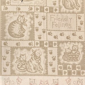 May include: A beige fabric with a patchwork design featuring cats and paw prints. The text "Friendly Felines" is printed in the center of the fabric.