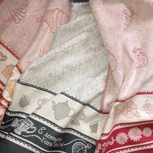 May include: Three kitchen towels with different designs. The first towel has a red and white border with a house and heart pattern. The second towel has a black and white border with a teacup and teapot pattern. The third towel has a red and white border with a floral pattern. The text on the second towel reads "E' sempre l'ora del te".