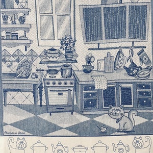 May include: A blue and white kitchen themed tea towel with a cat, a mouse, and a variety of kitchen utensils. The towel has a checkered pattern and the text "Prodotto in Italia" at the bottom.
