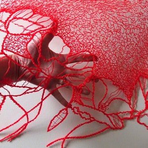 Puede incluir: Encaje rojo impreso en 3D con un delicado patr&oacute;n floral. El encaje es transl&uacute;cido y una mano lo sostiene.