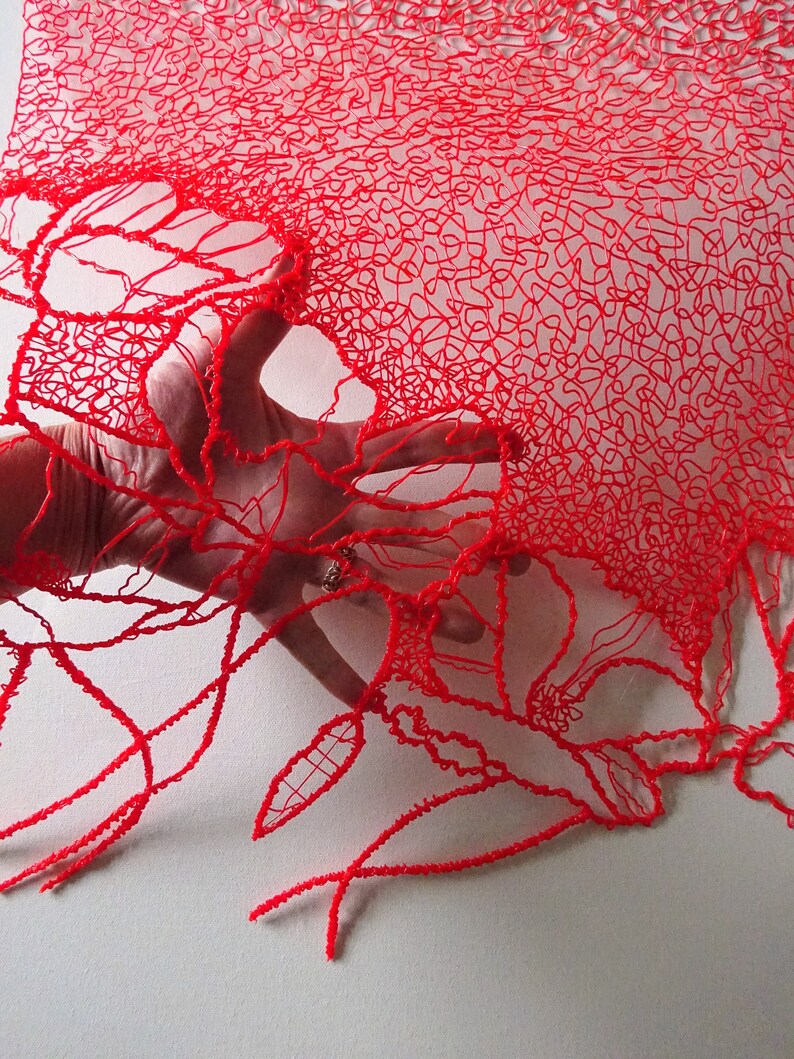 Puede incluir: Encaje rojo impreso en 3D con un delicado patr&oacute;n floral. El encaje es transl&uacute;cido y una mano lo sostiene.