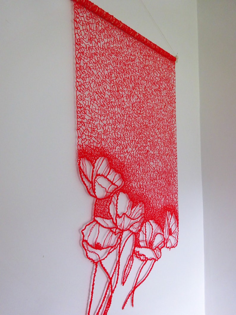 Puede incluir: Colgante de pared de arte de hilo rojo con un dise&ntilde;o de amapolas. El arte de hilo est&aacute; hecho con hilo rojo y se cuelga en una pared blanca.