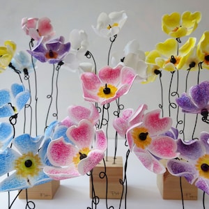 May include: A bouquet of colourful paper flowers with textured surfaces. The flowers are arranged in a vase and are made of different colours, including blue, pink, yellow, and purple.