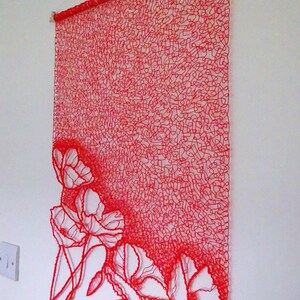 Puede incluir: Un tapiz de pared de arte de hilo rojo con un dise&ntilde;o de flores. Las flores est&aacute;n hechas de intrincados bucles de hilo rojo.