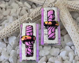 May include: A pair of silver dangle earrings with rectangular pink and black glass panels and a silver accent. The glass panels have a metallic finish and a swirl pattern.