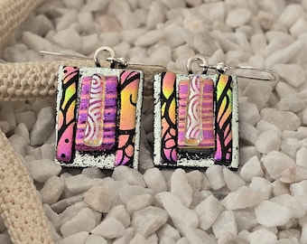 May include: A pair of square earrings with silver hooks. The earrings feature a colorful design with pink, yellow, and purple hues. The design includes vertical stripes and a decorative pattern. The earrings are set against a white background.