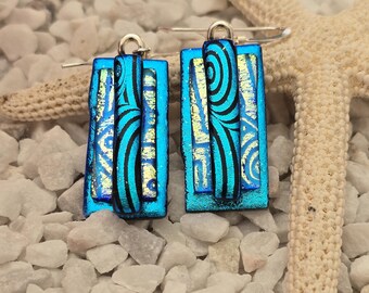 May include: A pair of blue and silver glass earrings with a geometric pattern. The earrings are rectangular in shape and have a silver hook closure.