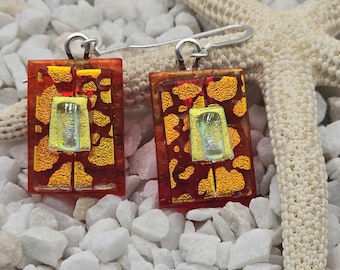 May include: A pair of red and gold glass earrings with a silver hook. The earrings are square shaped and have a geometric pattern.