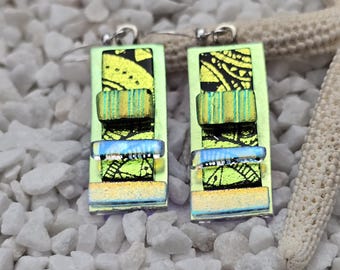 May include: A pair of green and black glass earrings with silver hooks. The earrings are layered with different colored glass pieces and have a black and white patterned design.