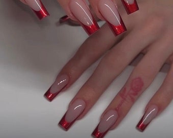 May include: Long, square-shaped nails with a nude base and a red tip. The red tips are a thin line along the edge of the nail, creating a French manicure look.