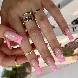 May include: Pink and white long square shaped acrylic nails with a white heart design on the ring finger nails.