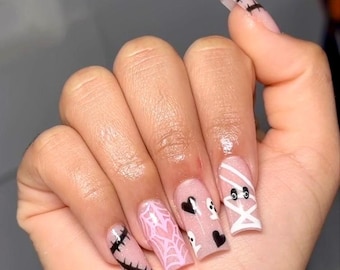 May include: A hand with long, square-shaped, pink acrylic nails decorated with Halloween-themed designs. The designs include a stitched nail, a spiderweb, ghosts, hearts, and mummy bandages. The thumb nail has black stripes.